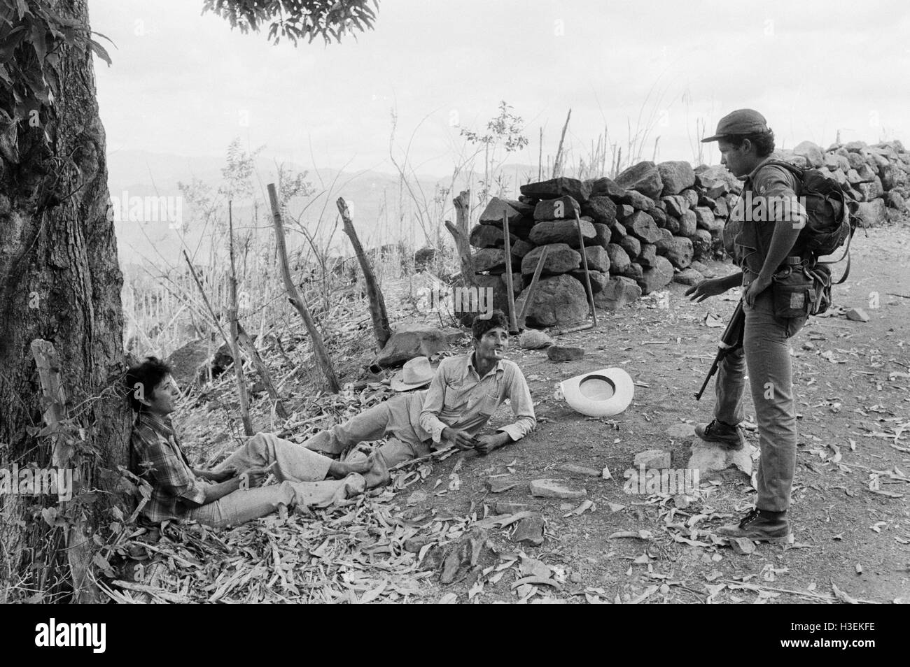 CHALATENANGO,  EL SALVADOR, FEB 1984: - Within the FPL Guerrilla's Zones of Control.  An FPL fighter stops to talk to two campasinos resting in the mididay heat. Stock Photo