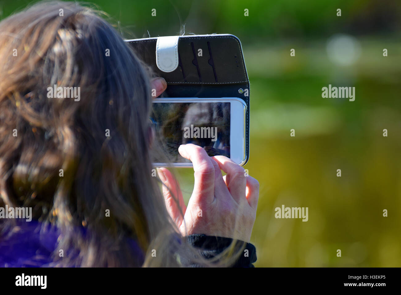 Woman taking a picture with her smart phone. Touch screen as a mirror, showing part of her faces. Stock Photo