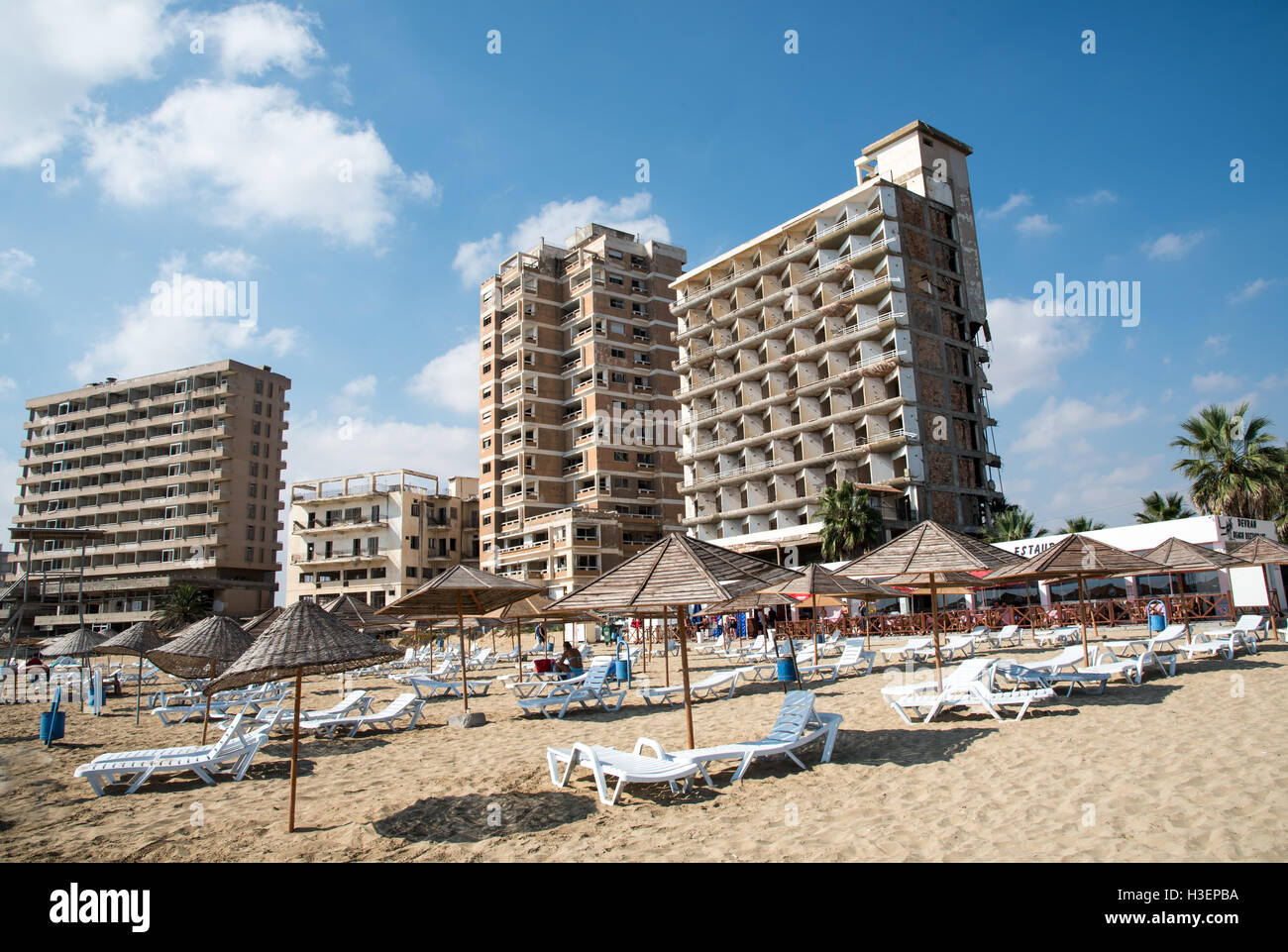 Palm Beach with beach umbrellas and tourists and the abandoned hotels at Varosha ghost  town, Famagusta, Northern Cyprus Stock Photo