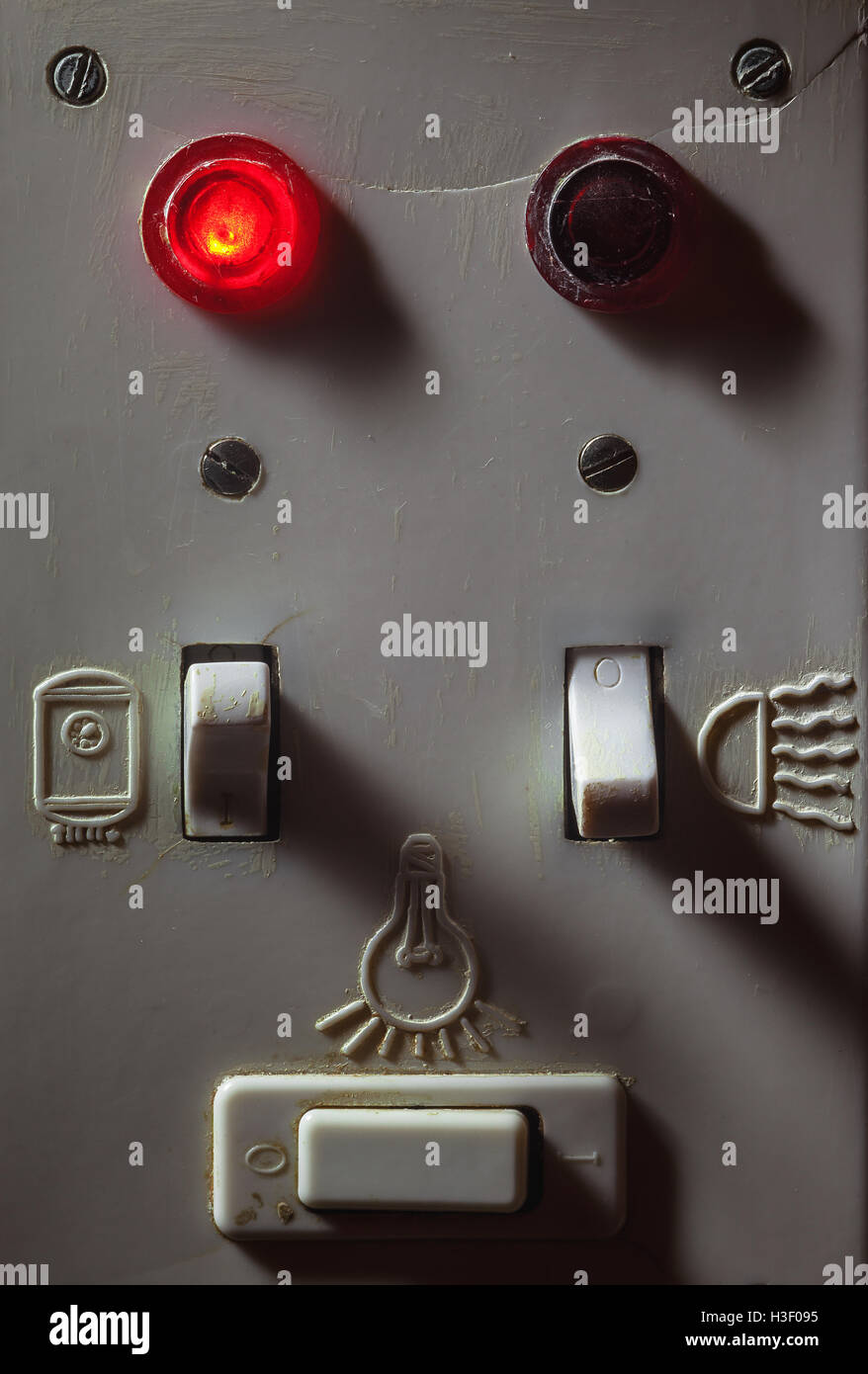 Details of an old dirty plastic switches for bathroom, red light is on for boiler. Stock Photo