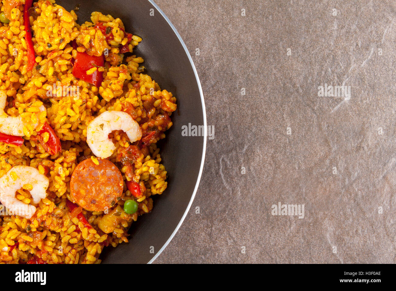 Freshly cooked chorizo, chicken and king prawn paella in a frying pan on a stone work surfce with copyspace Stock Photo
