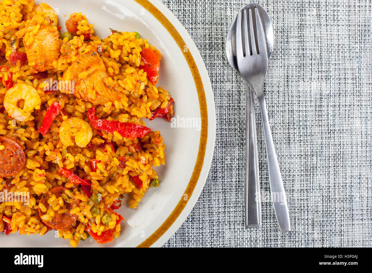 Plated chorizo, chicken and king prawn paella with a spoon and fork on a woven table mat Stock Photo
