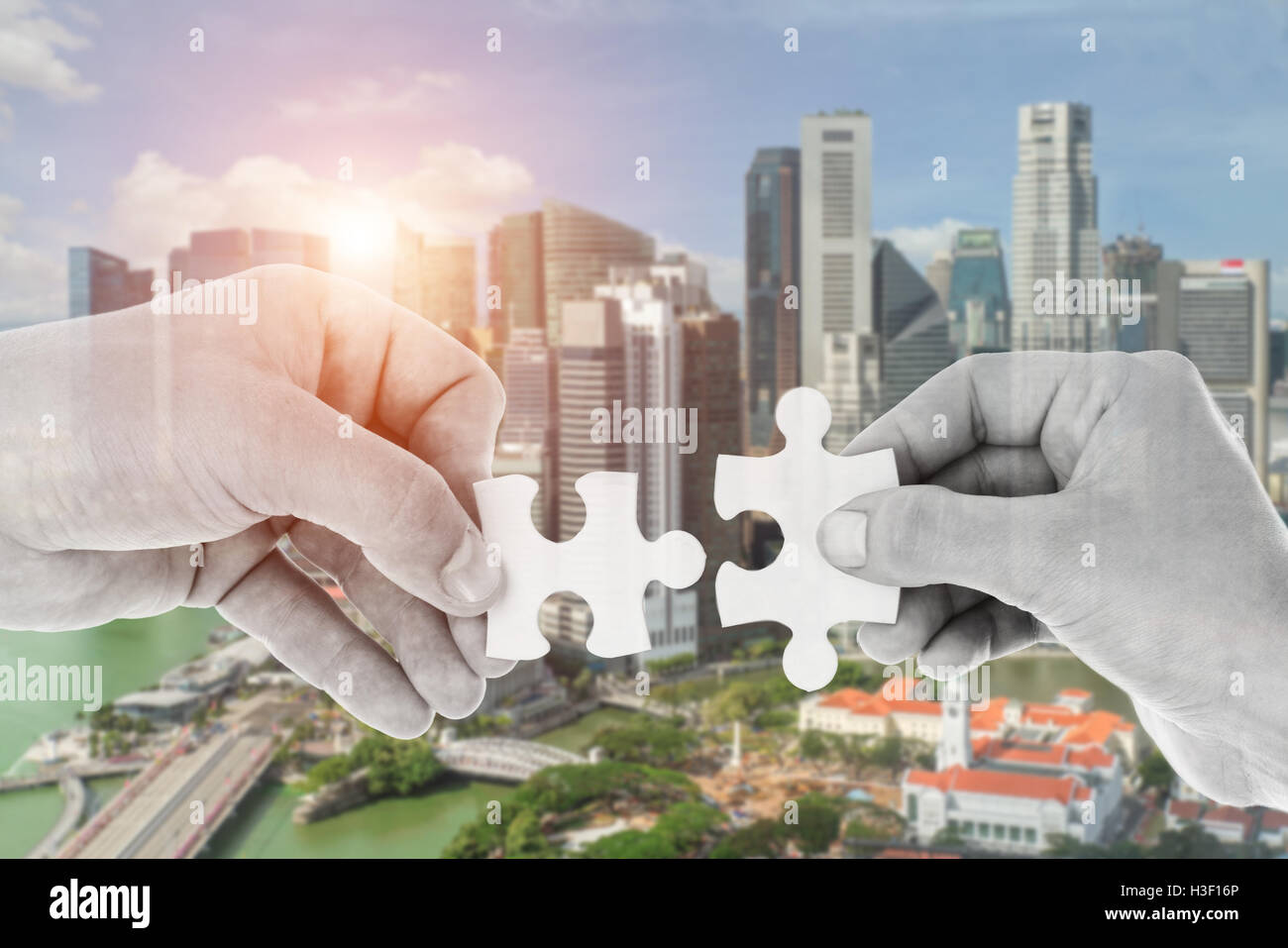 Hands putting partnership puzzle pieces together on skyscraper building in background. Partnership network concept Stock Photo