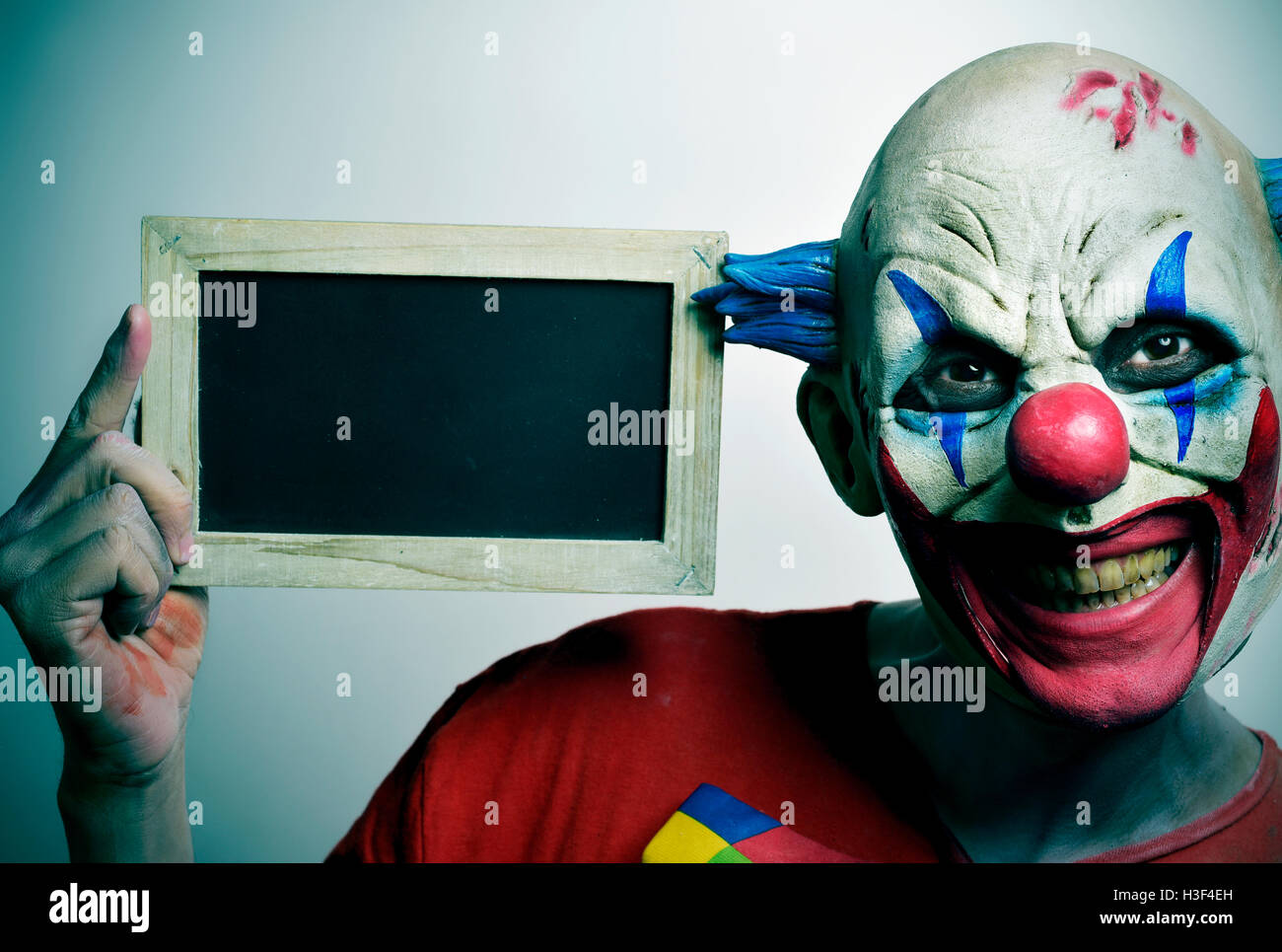 portrait of a scary evil clown with a blank wooden-framed chalkboard Stock Photo