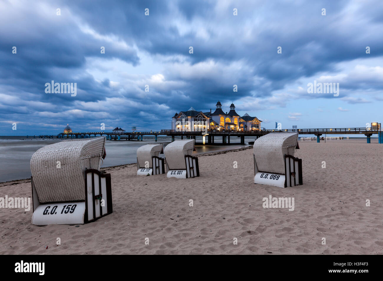 Beach chairs in front of the illuminated pier of Baltic Sea resort Sellin, Ruegen, at dusk Stock Photo