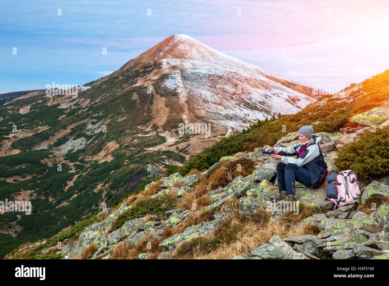 Female Hiker sitting on green Stone and using Thermos Stock Photo