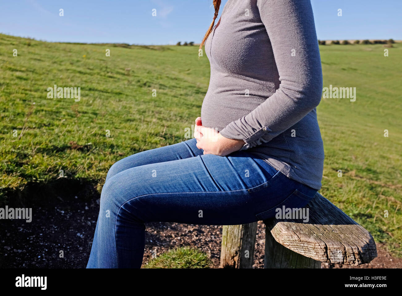 Young pregnant woman in her 20s takes a rest on park bench as she holds her stomach Stock Photo