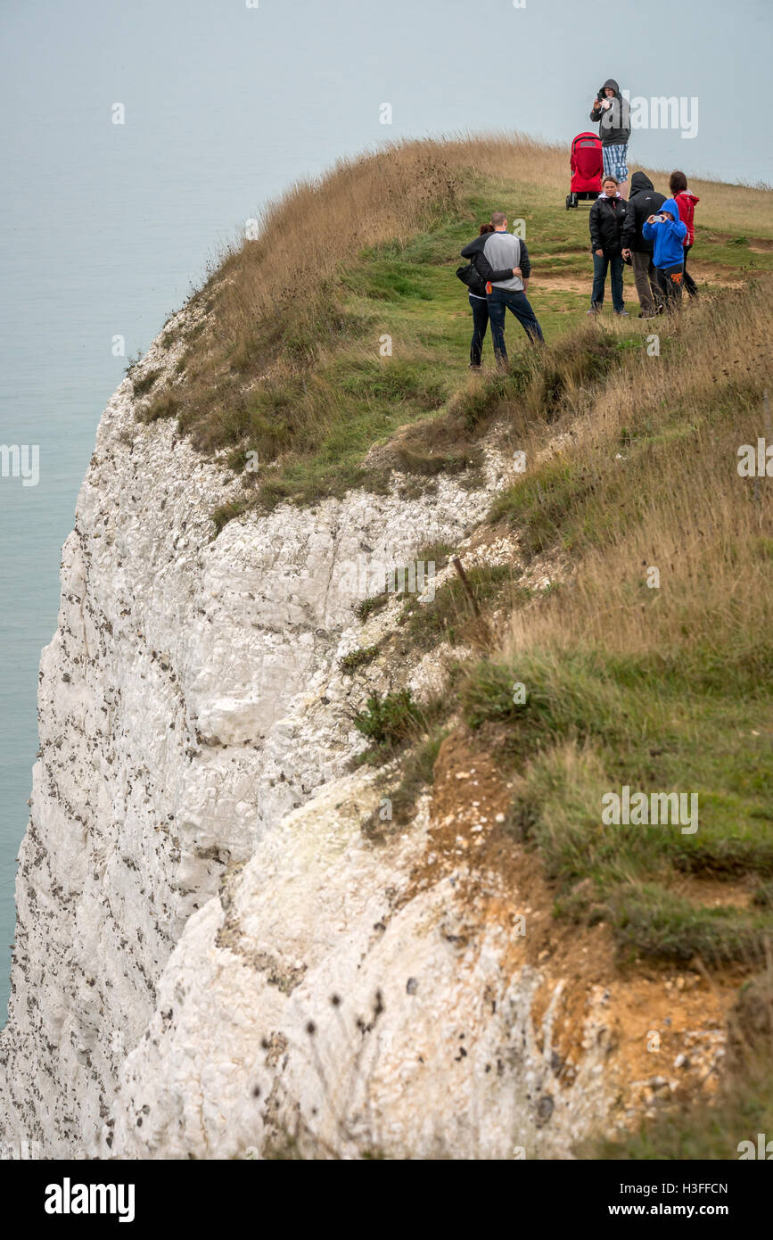 Daytrippers risk their lives posing for photographs on the cliff edge at Beachy Head Stock Photo