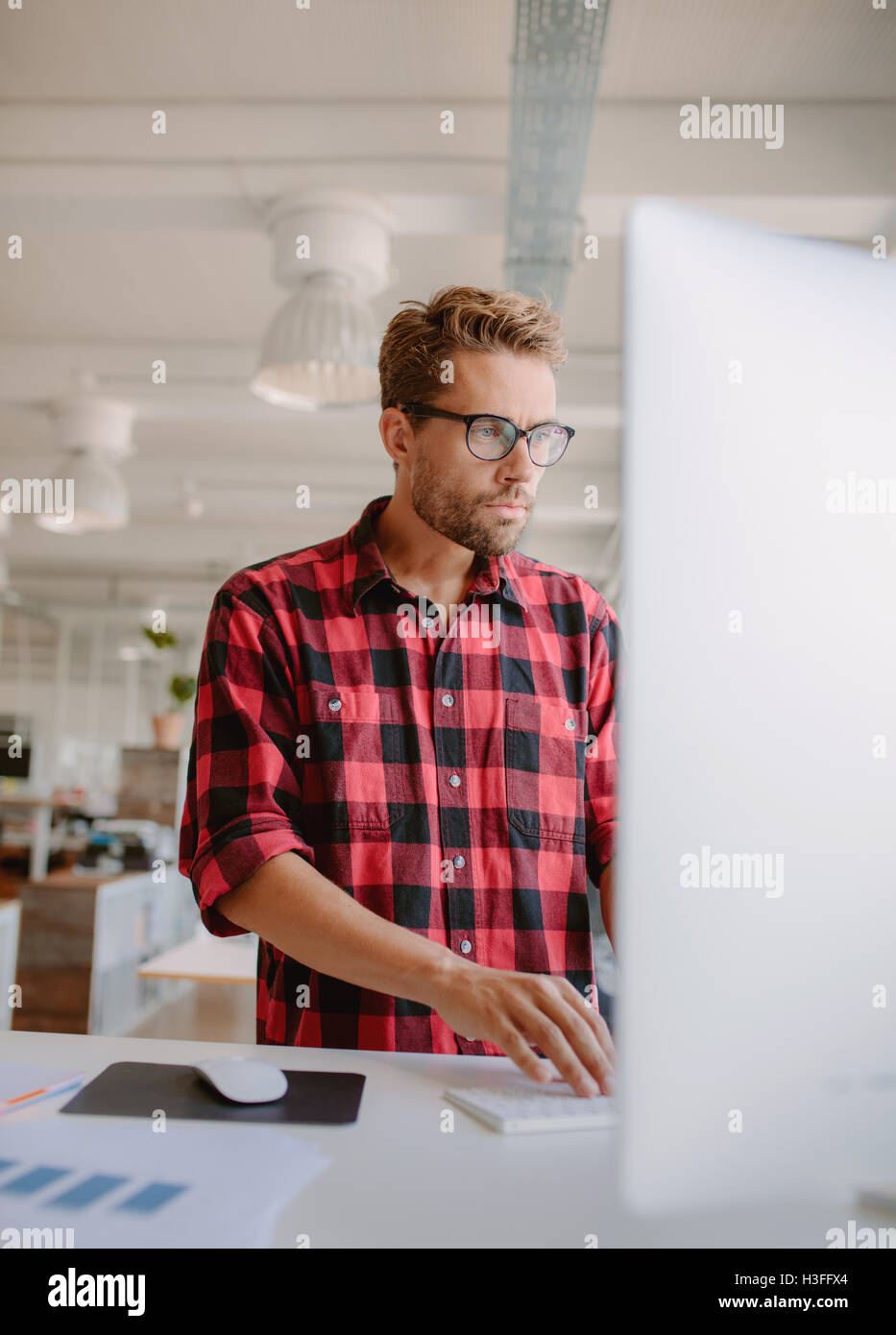 Vertical shot of young man working on computer. Businessman concentrating on his work in modern office. Stock Photo