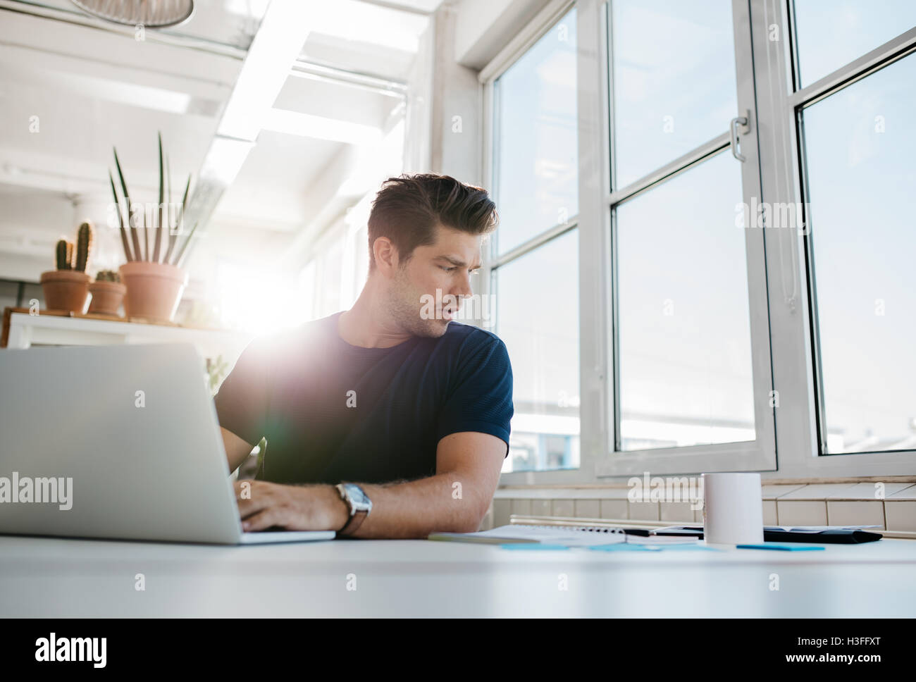 Shot of young businessman working on at his desk, using laptop and looking at documents on table. Stock Photo