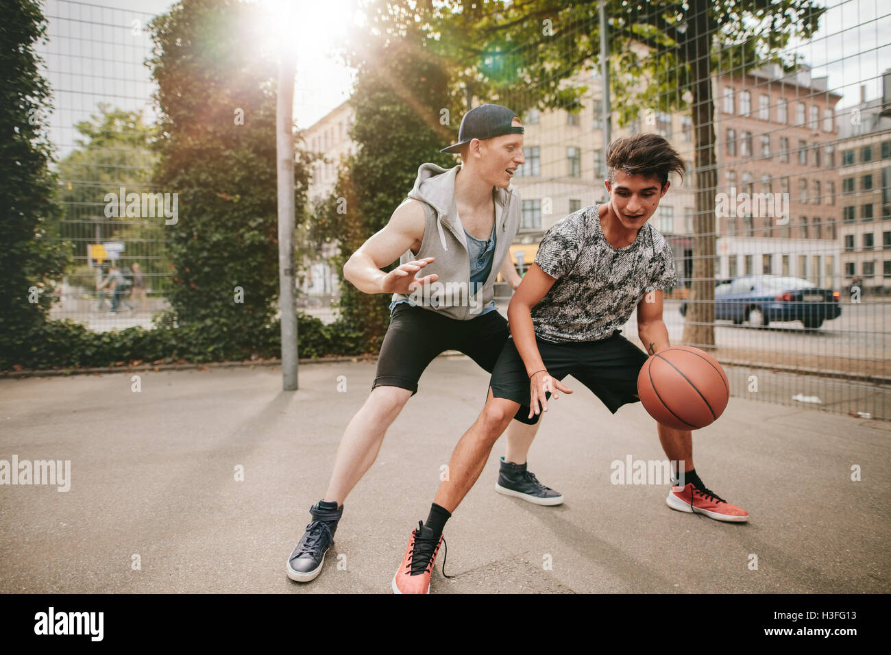 Teenagers playing basketball on outdoor court and having fun. Young man dribbling basketball with friend blocking. Streetball ga Stock Photo