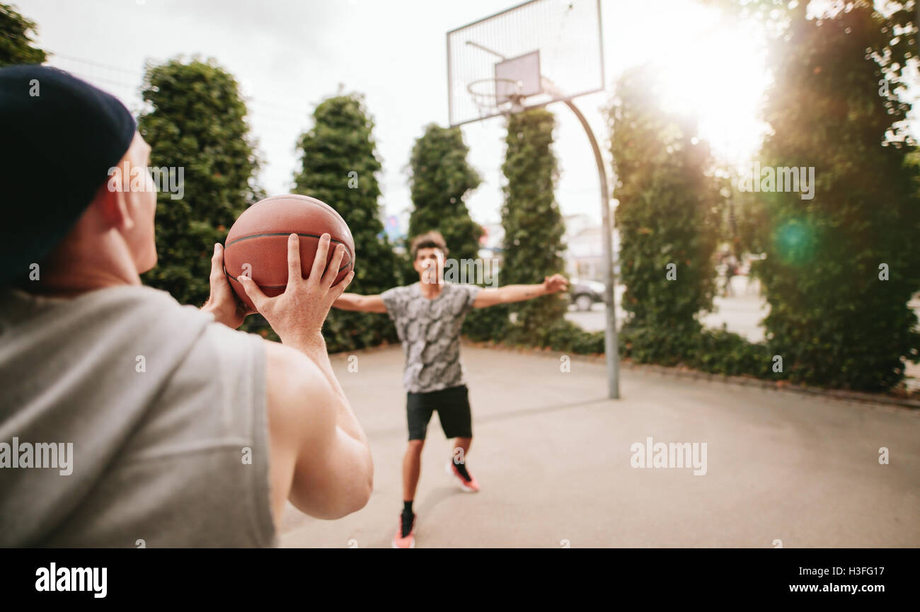 Young man taking shot with friend blocking on basketball court. Streetball players on court playing basketball. Stock Photo