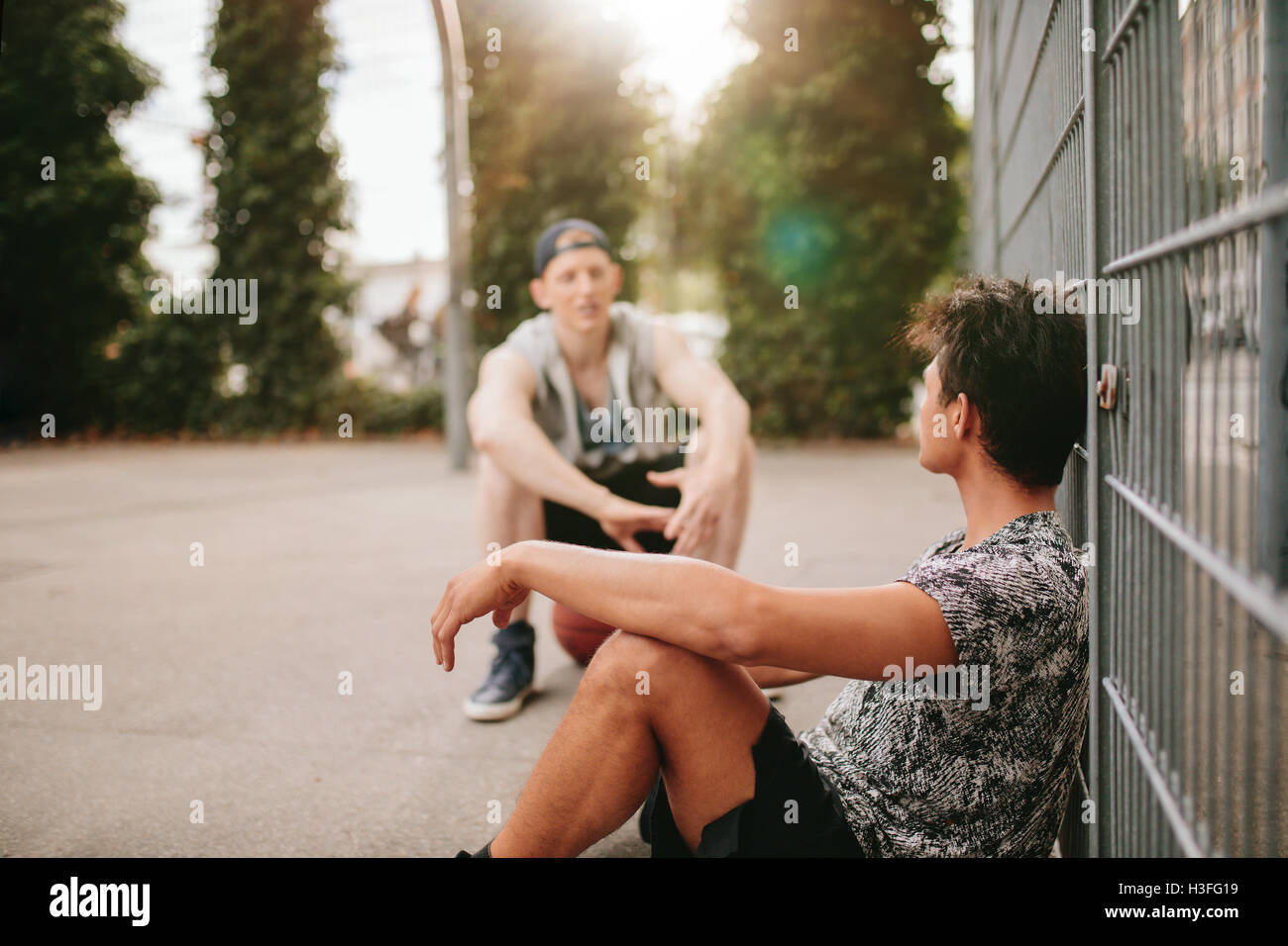 Young man relaxing on basketball court with a friend. Streetball players taking break after playing a game. Stock Photo