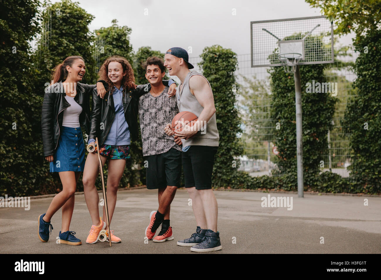Full length shot of multiracial group of people enjoying outdoors on basketball court. Four young friends standing together and Stock Photo