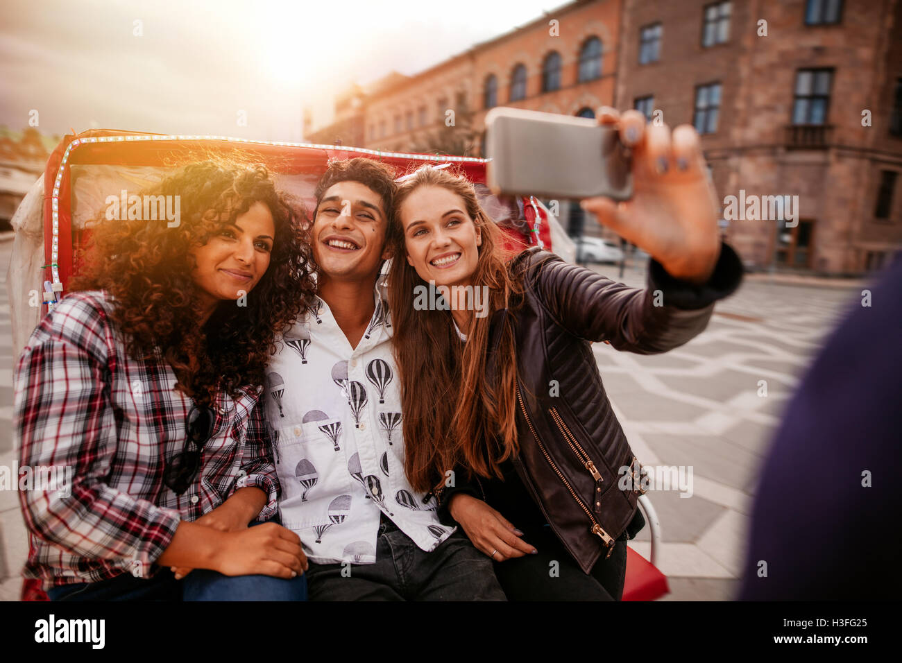 Teenage friends taking selfie on tricycle. Young man and women riding on tricycle bike and taking self portrait. Stock Photo