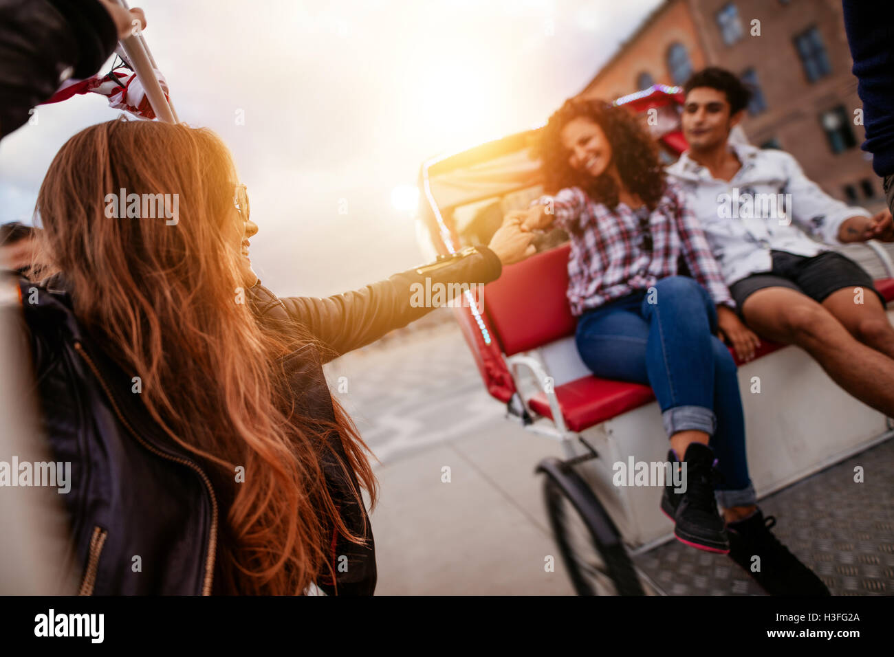 Young people enjoying tricycle ride in the city. Teenagers riding on tricycle on road, with woman holding hand of female friend. Stock Photo