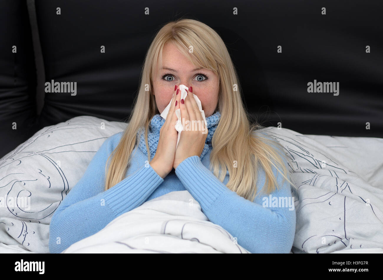 Sick woman blowing her nose in bed sitting propped up against the