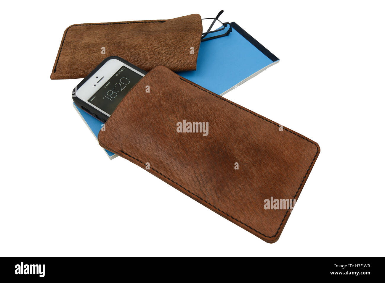 Handmade, brown leather mobile case and glasses case, with spectacles with a blue cheque book. Isolated against a white background. Stock Photo