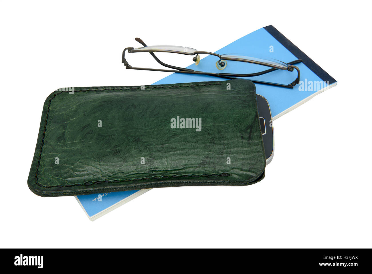 Handmade, green leather mobile phone case and spectacles with a blue cheque book. Isolated against a white background. Stock Photo