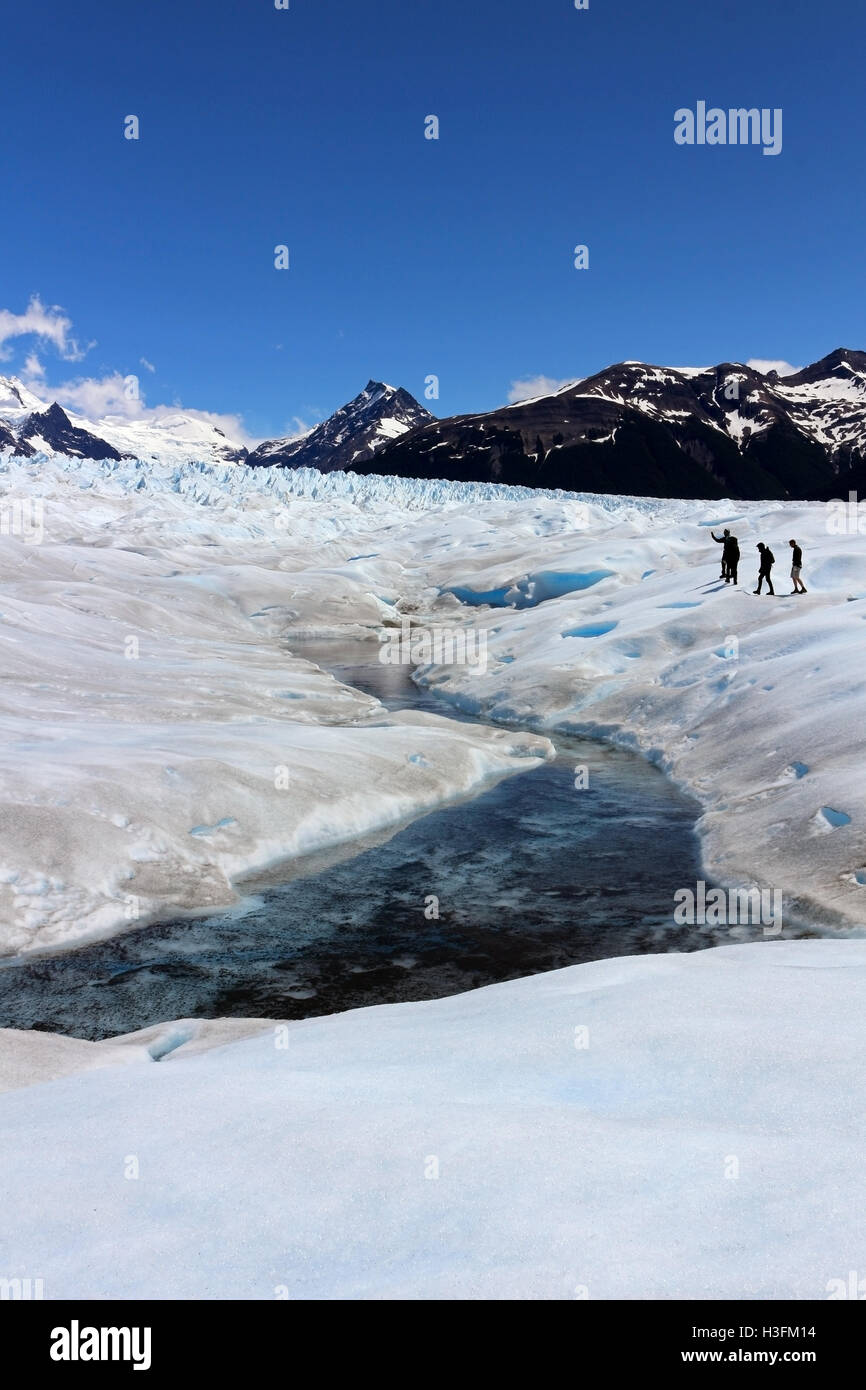 People exploring Perito Moreno glaciar near a little river formed by summer ice melting with a typical blue color Stock Photo