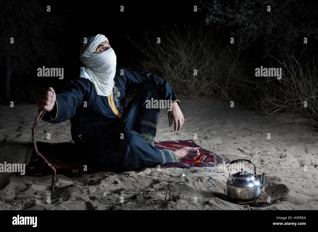 Man in traditional Tuareg outfit in a desert, preparing tea Stock Photo
