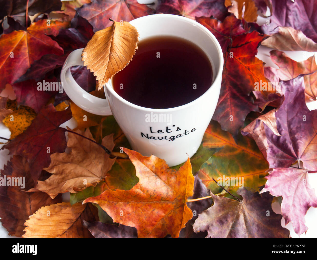 Beautiful and colorful autumn leaves and white cup of tea standing on a table made of wooden planks Stock Photo