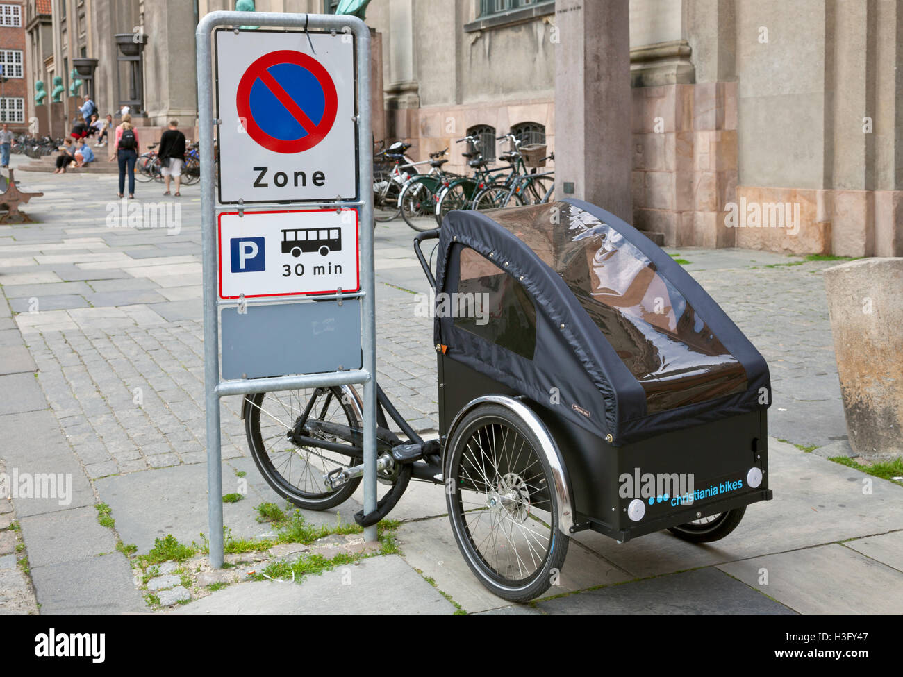 Christiania cargo bicycle parked and locked outside Copenhagen University at parking zone sign allowing coaches to park 30 minutes only. Copenhagen Stock Photo