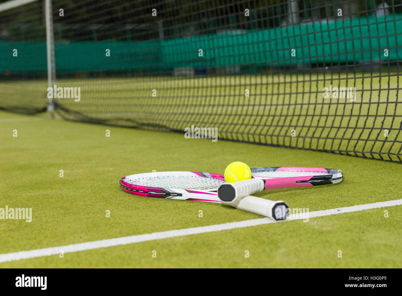 Two tennis rackets with a tennis ball lying near net on a green grass court outdoors in summer or spring Stock Photo