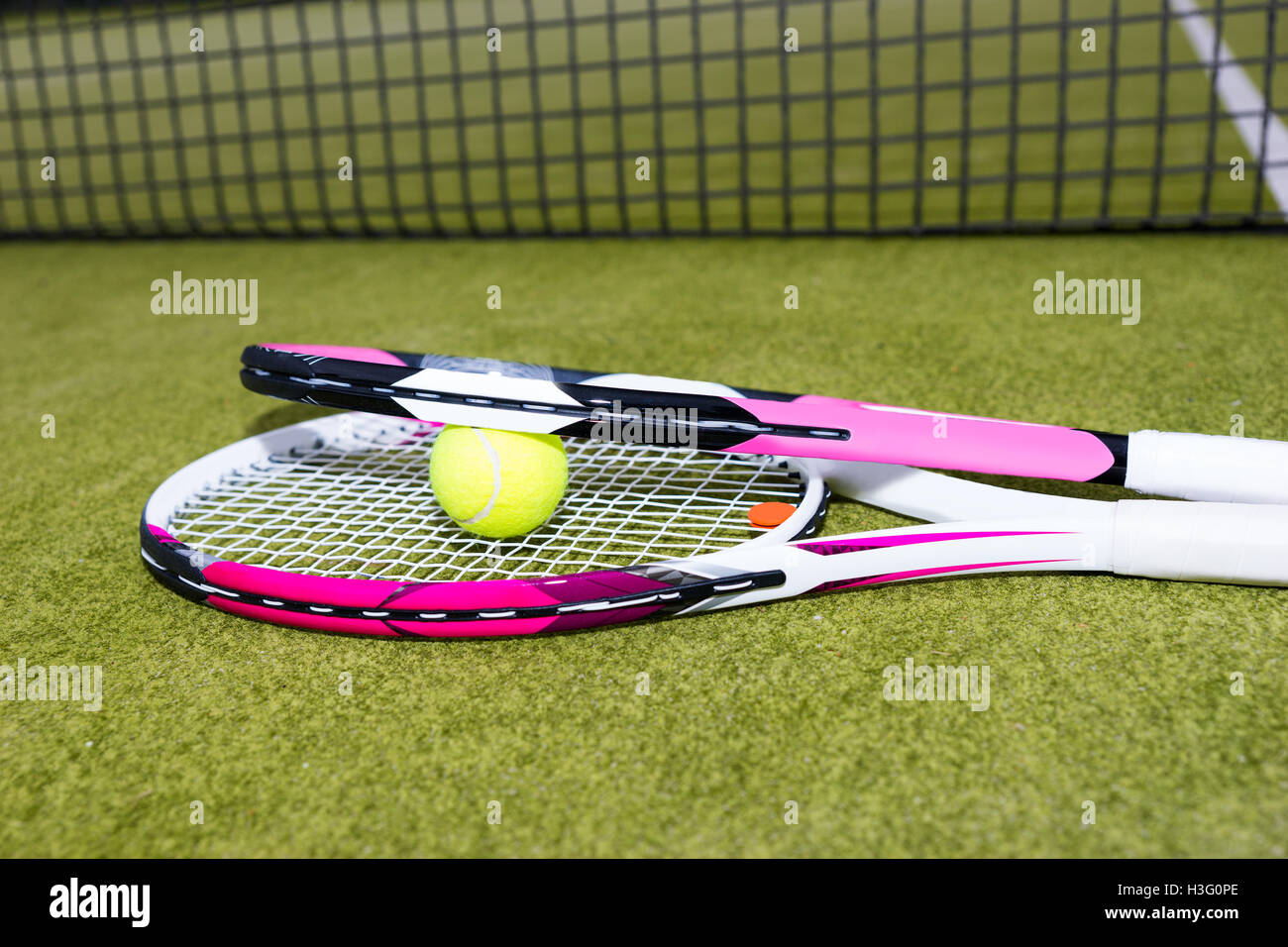 Sporty pink tennis rackets with ball on green background lying near net ...
