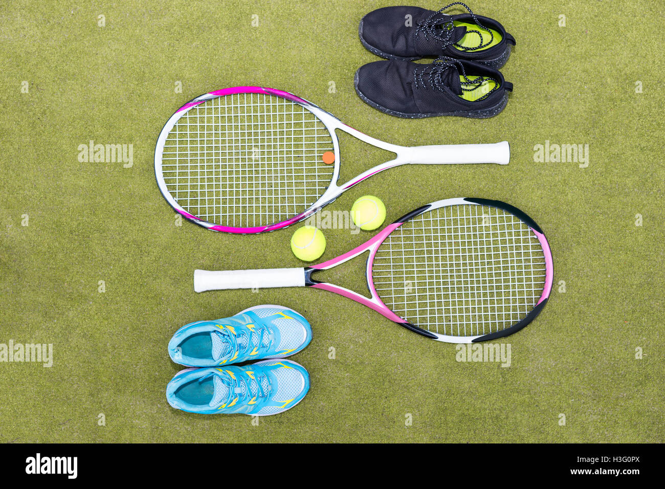 Tennis equipment set of two tennis rackets, two balls, male and female sneakers on green grass court Stock Photo