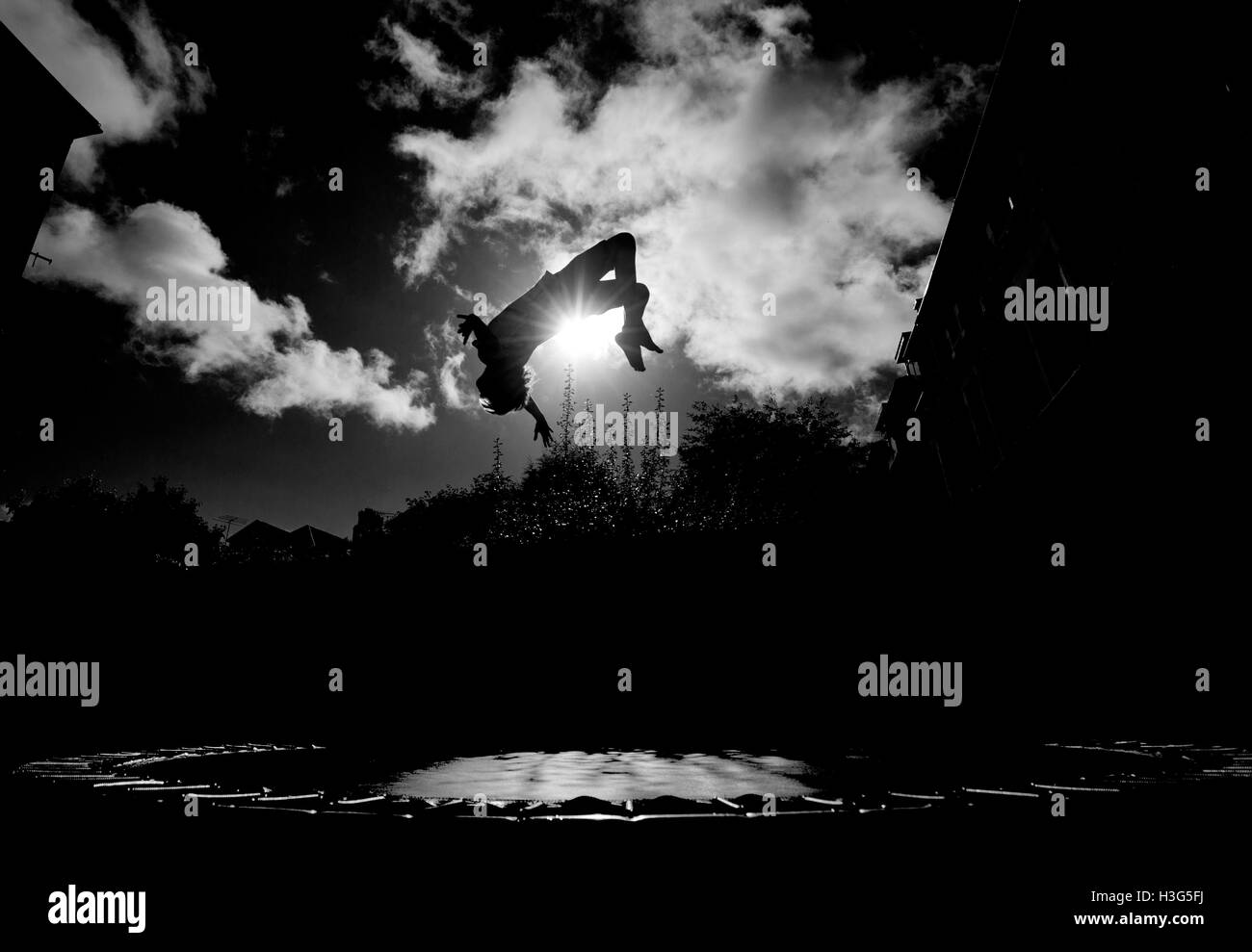 Boy in silhouette, upside down while trampolining in an urban garden against a bright sun.  *Can be model released on request of Stock Photo