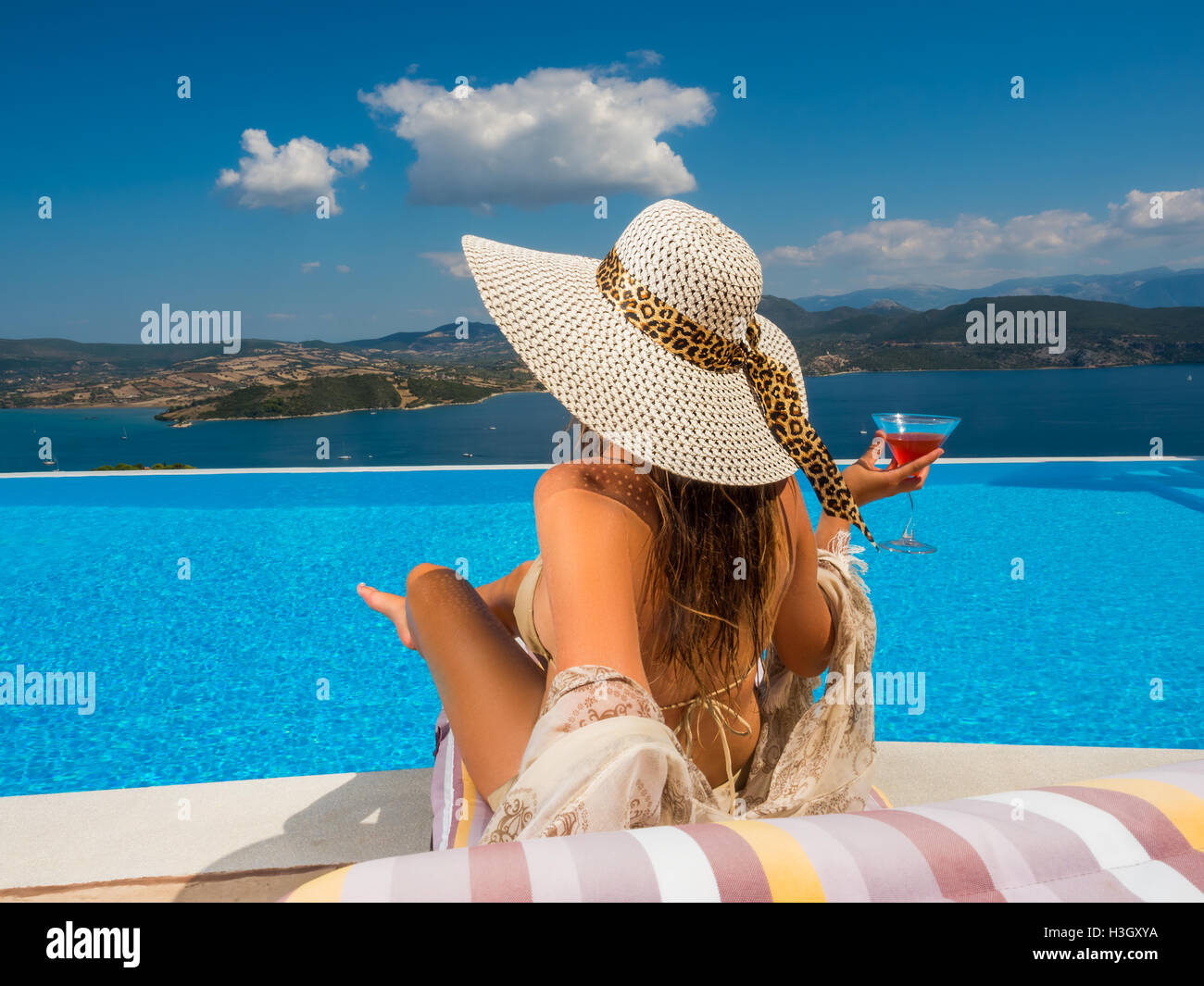 Beautiful woman with a hat is relaxing in an infinity pool with a ...