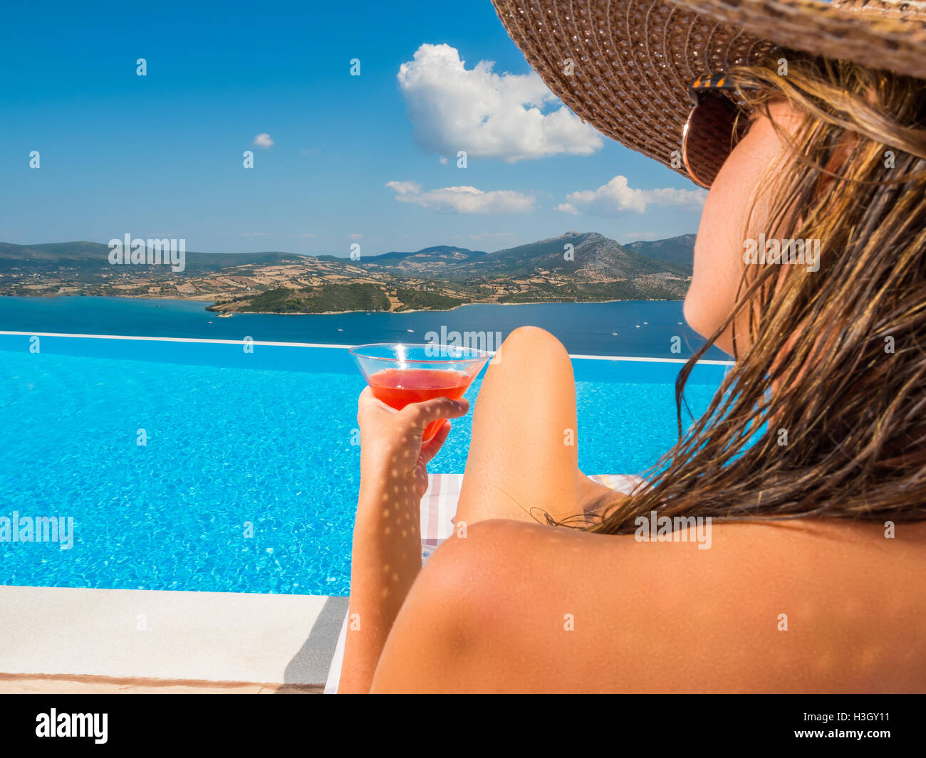 Beautiful woman with a hat is relaxing in an infinity pool with a ...