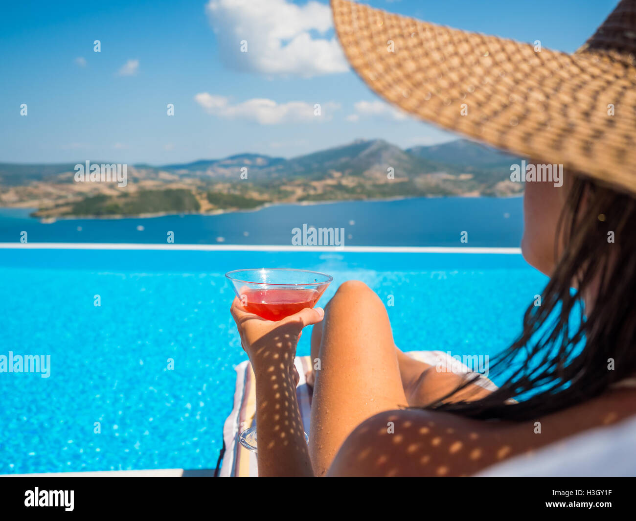 Beautiful woman with a hat is relaxing in an infinity pool with a ...