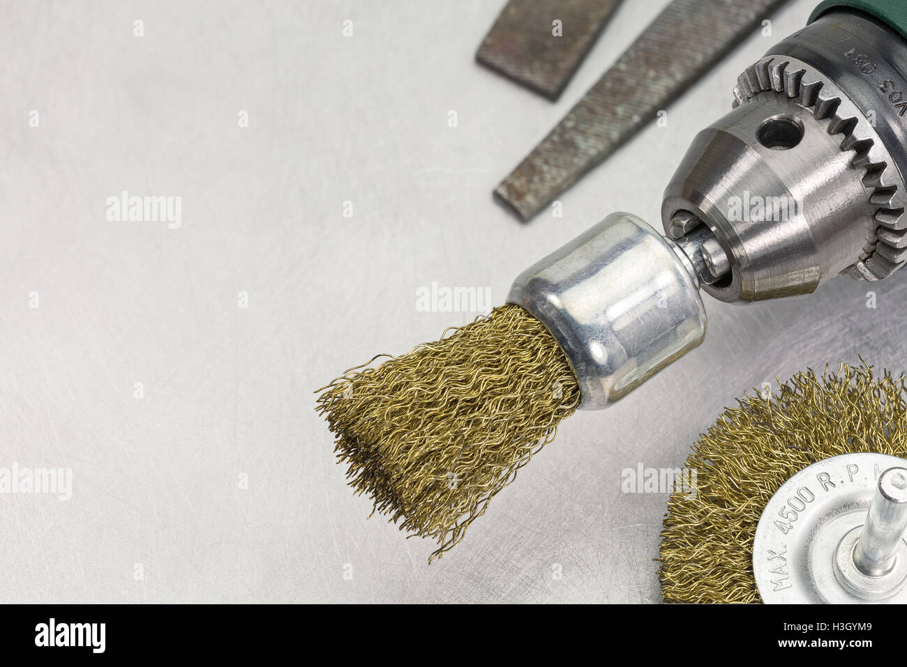 Power drill head with rotating brass brushes on scratched metal