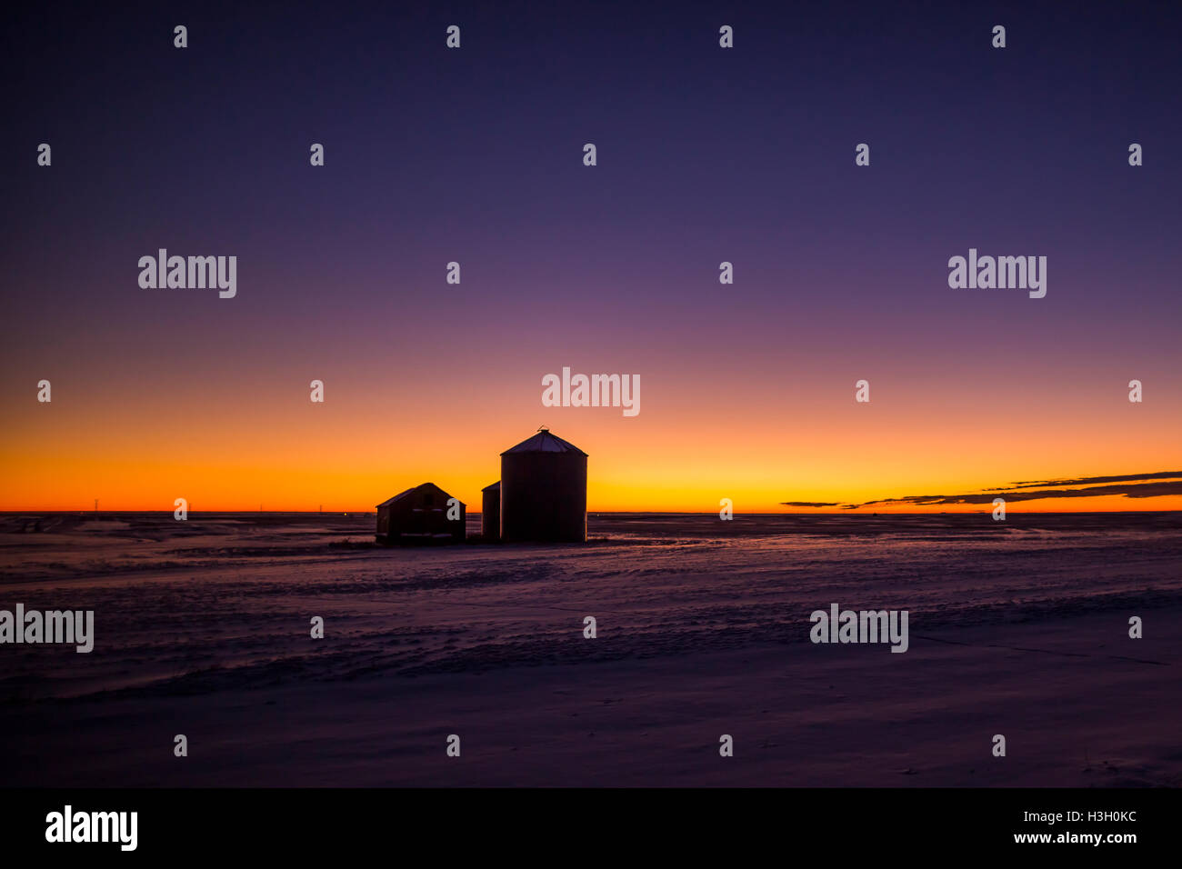 Dawn glows behind farm buildings on a cold morning on the prairies east of High River, Alberta, Canada. Stock Photo