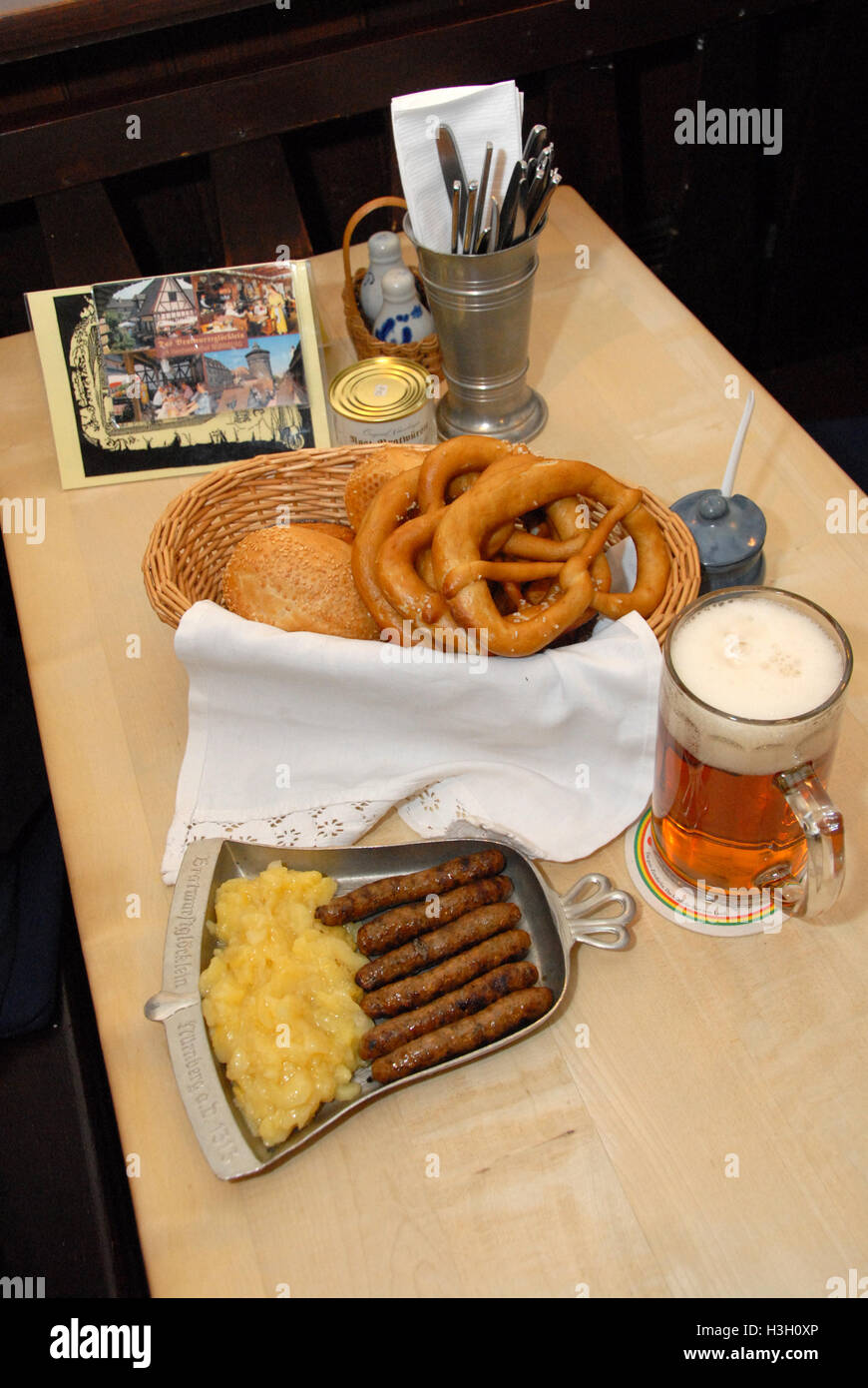The famous finger-thin Nuremberg Bratwurst (Nuremberg sausage) accompanied with German bread, potato salad on a pewter plate and a half-litre glass of Stock Photo