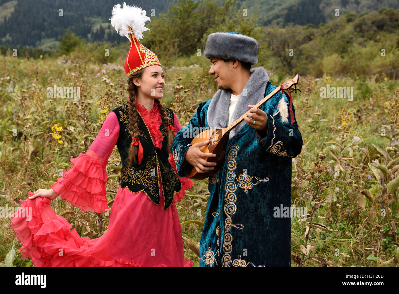 Man playing dombra and woman in traditional Kazakh dress in a field at Huns village Kazakhstan Stock Photo