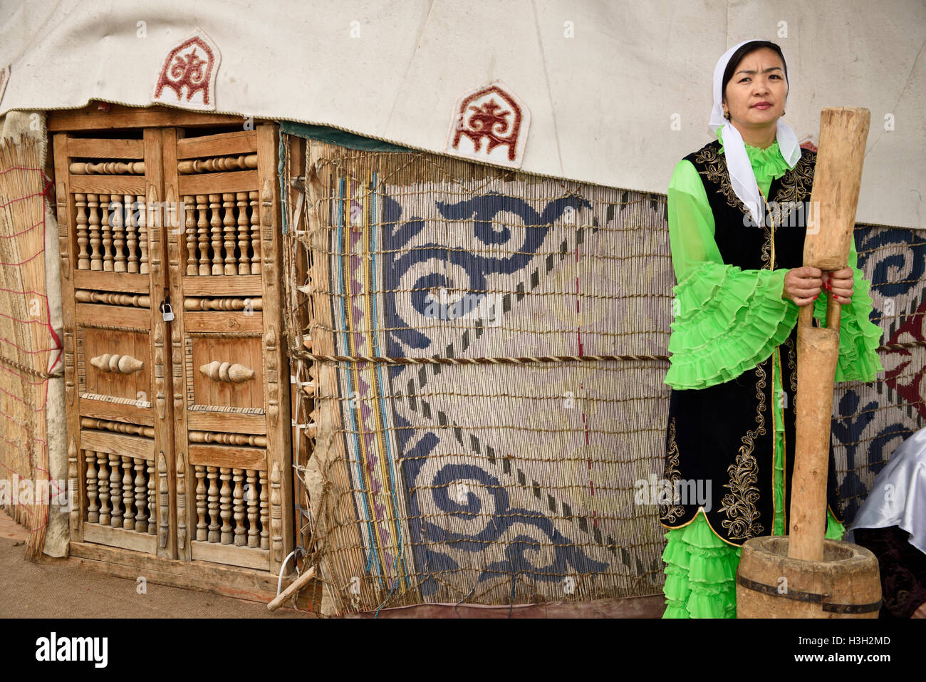 Woman in traditional Kazakh dress grinding wool for felt next to a yurt at Huns village Kazakhstan Stock Photo