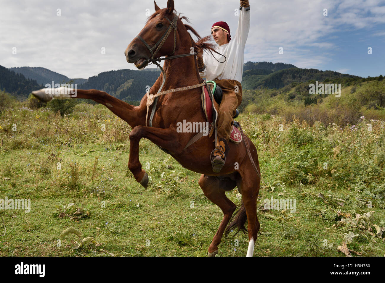 Kazakh horse rider raising arm on rearing gelding in Huns village Kazakhstan Stock Photo