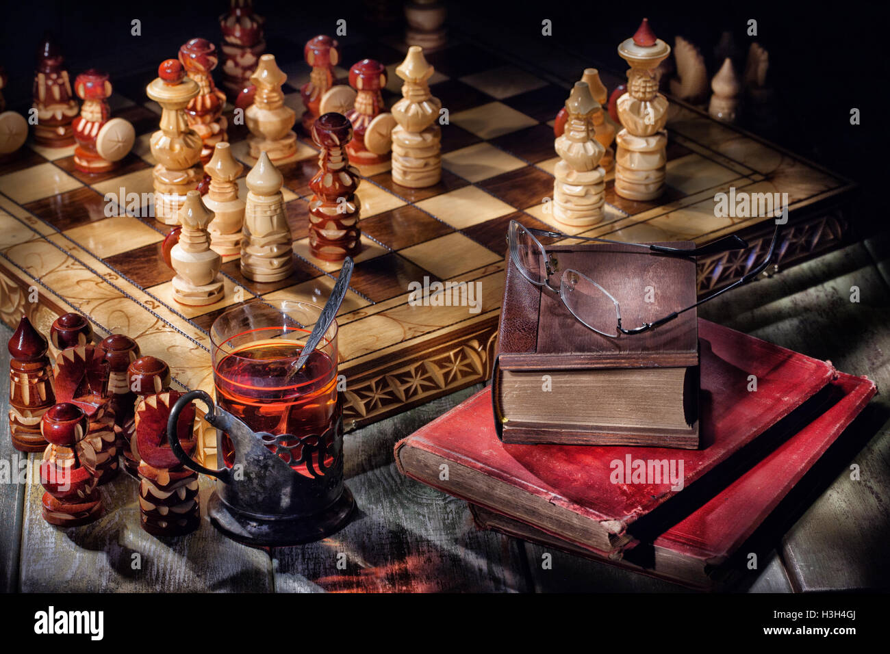 Wooden crafted chess, old books and glass of tea Stock Photo