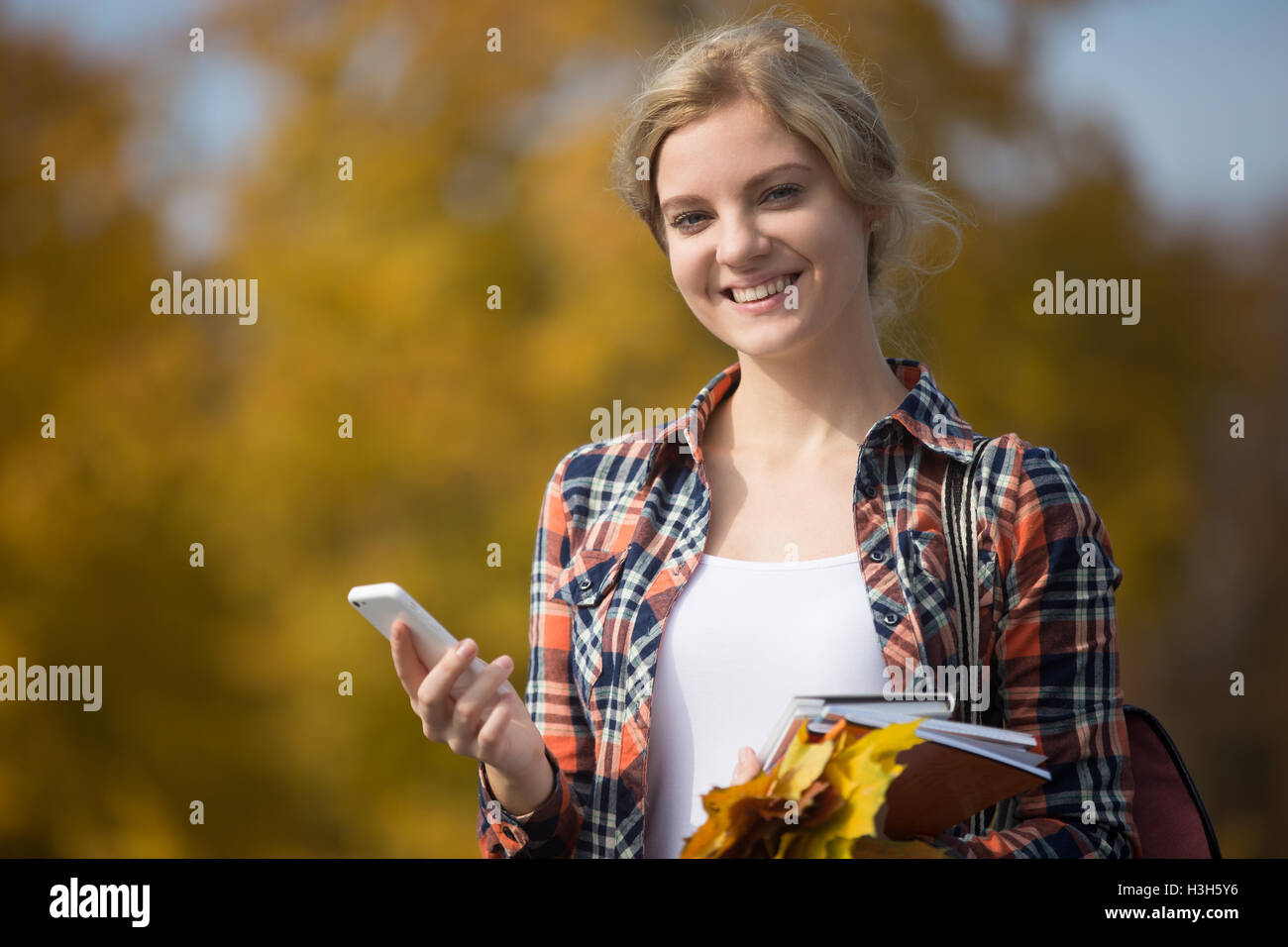 Portrait of student outsides, holding mobile phone in one hand Stock Photo