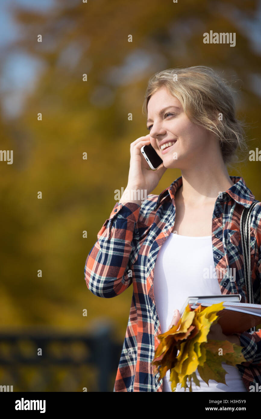 Portrait of a young smiling student outsides, talking on phone Stock Photo