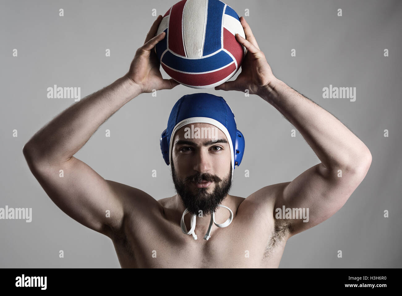 Happy professional water polo player holding ball over his head looking