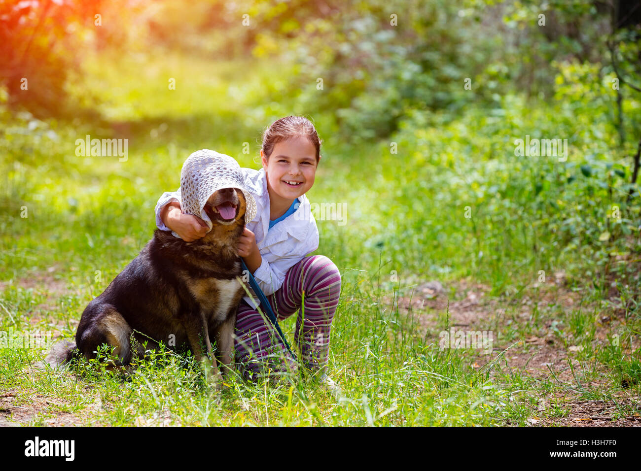 Happy little girl playing with dog wearing summer hat in the forest ...