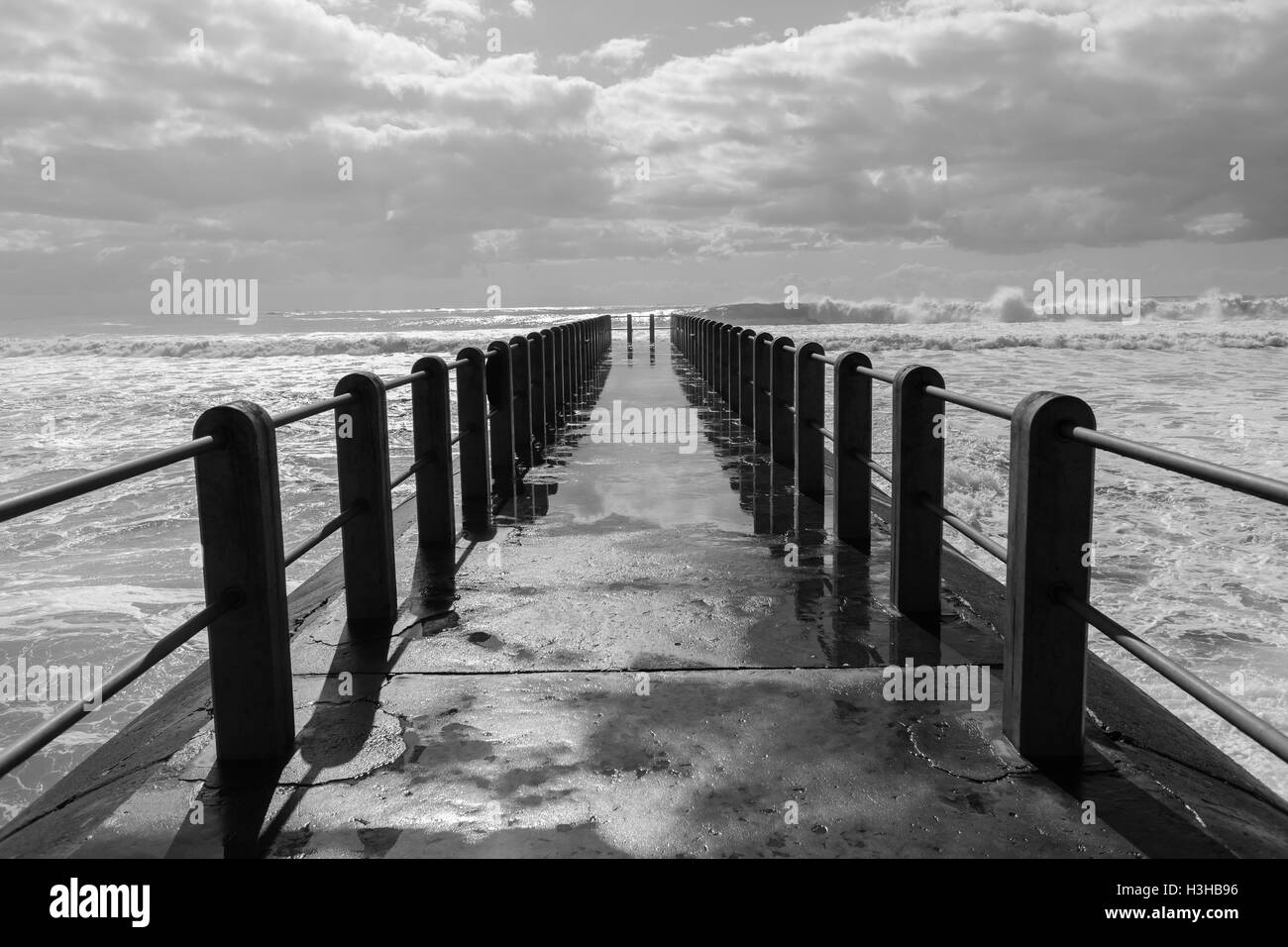 Beach pier jetty with ocean storm waves crashing with water power. Stock Photo