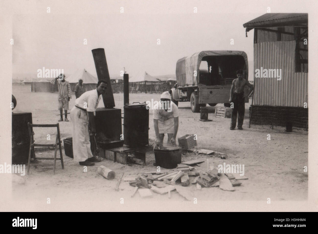 Unidentified Egyptian men preparing food on a wood fired cooking stove in a British army camp. Photo taken in 10 Base Ordnance Depot Royal Army Ordnance Corps (RAOC) camp at Geneifa Ismailia area near the Suez Canal 1952 Stock Photo