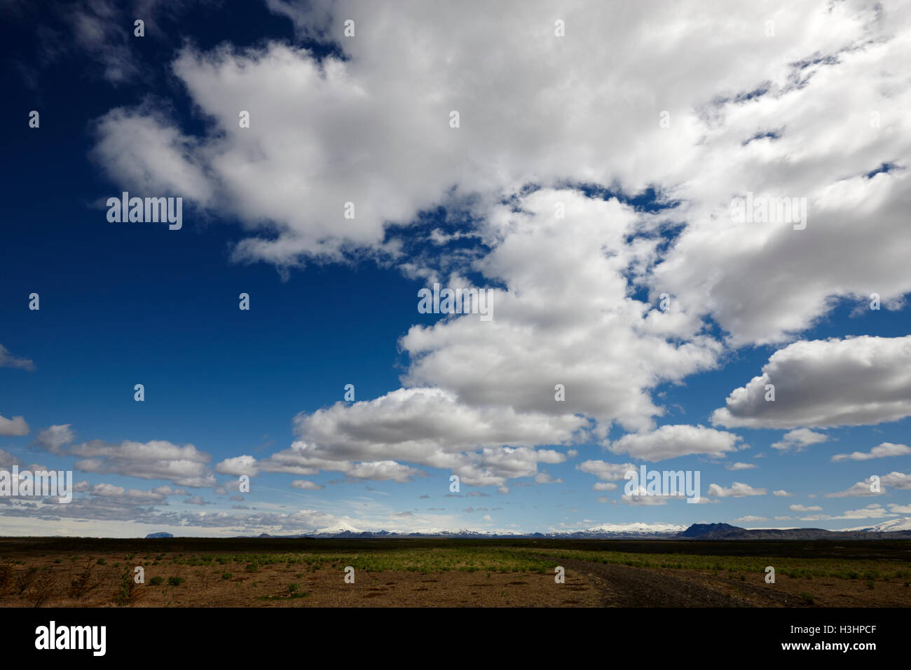 white clouds in blue sky over dirt track into the wilderness in open farmland in southern Iceland Stock Photo