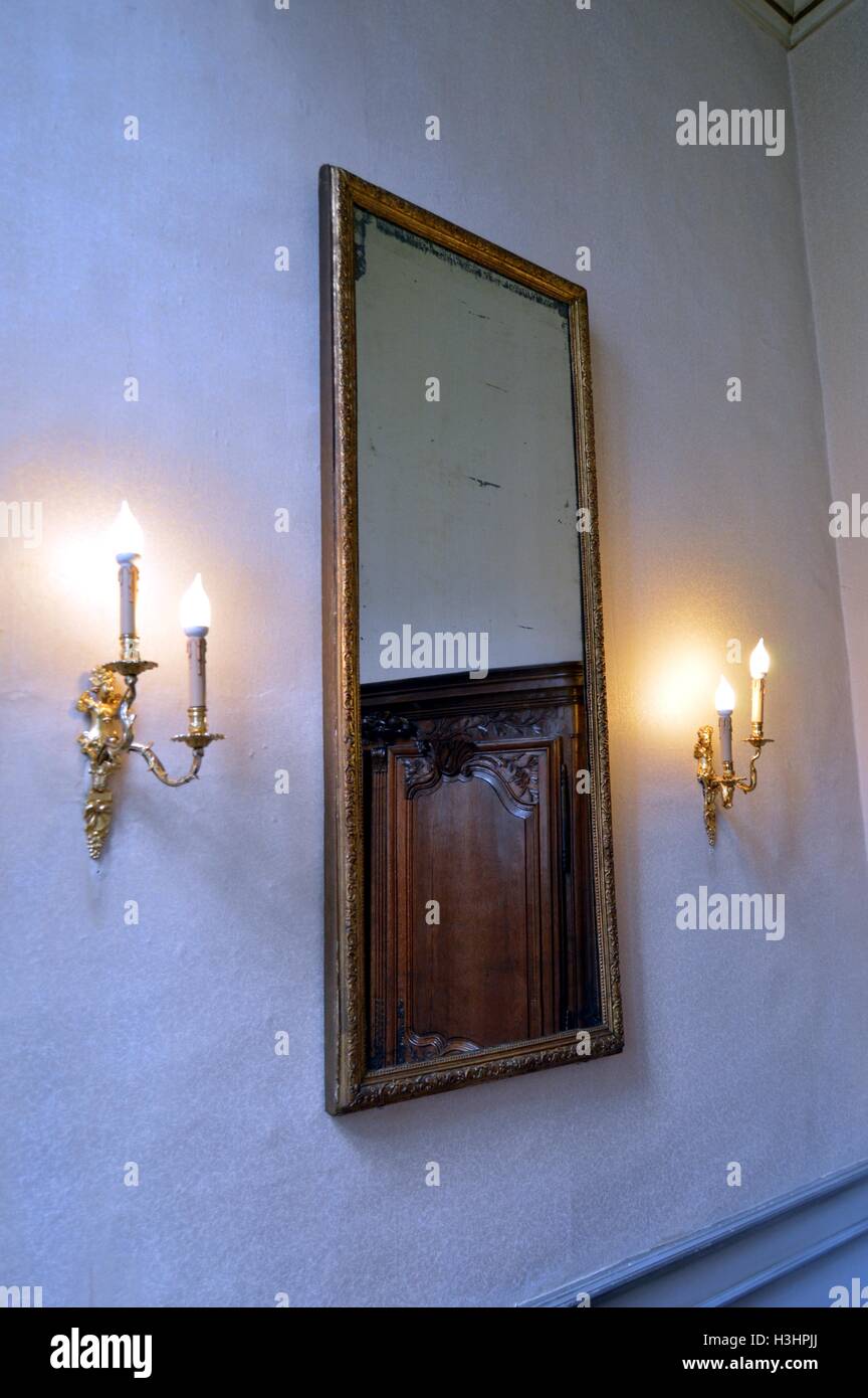 Old mirror on a white wall with two candlesticks. Stock Photo