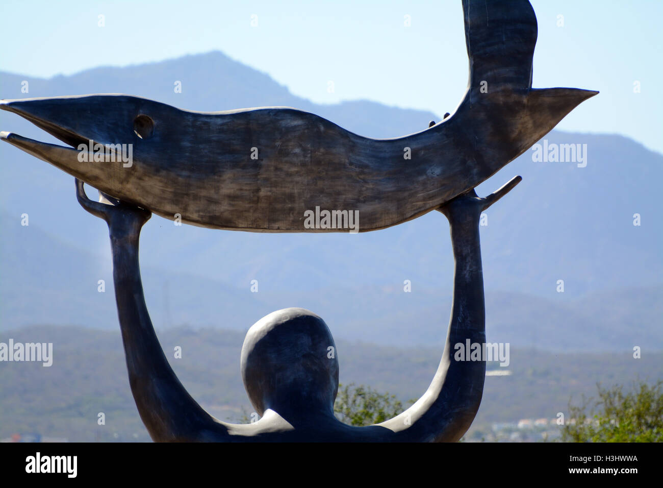 Close-Up Statue of a Man Holding a Fish Towards the Sun Heavens at Wirikuta Botanical Garden, Mexico with Mountains &  Blue Sky Stock Photo